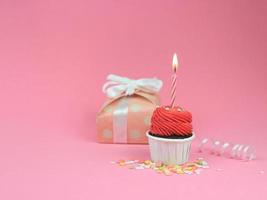 söt röd cupcake med rosett ljus och presentförpackning på rosa bakgrund med kopia utrymme. grattis på födelsedagen part bakgrund koncept. foto