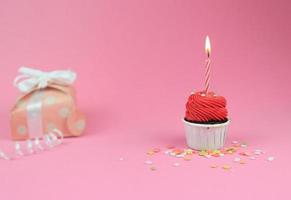 söt röd cupcake med rosett ljus och presentförpackning på rosa bakgrund med kopia utrymme. grattis på födelsedagen part bakgrund koncept. foto