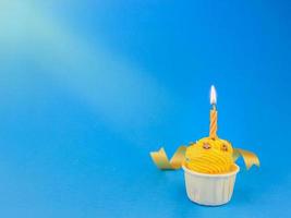 söt ljus gul cupcake med rosett ljus på blå bakgrund med kopia utrymme. grattis på födelsedagsfesten foto