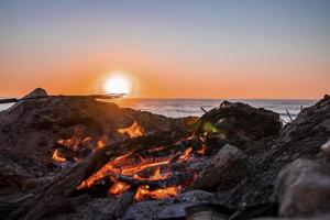 brasa med brinnande ved under vacker solnedgång på stranden foto