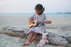 ung asiatisk tjej spelar ukulele på stranden. foto