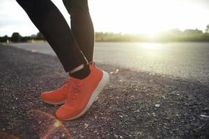 närbild fötter med löparskor stående på asfalten marken med naturligt orange ljus av solnedgången i bakgrunden foto