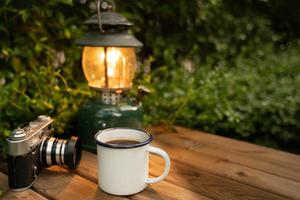 selektiv inriktning vit emalj kaffemugg och kaffeservis i trädgården med gamla lyktor i campingatmosfär. mjukt fokus. foto