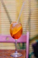 aperitifcocktail bestående av prosecco, aperol och sodavatten, står i vinglas på träbord i baren. aperol spiritz cocktail med flera iskuber och en skiva apelsin. foto
