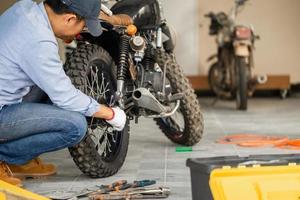 ung man fixar motorcykel i verkstadsgarage, man reparerar motorcykel i verkstad, mekanisk hobby och reparationskoncept foto