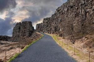 människor som går på vägen vid klippor mot mulen himmel i thingvellir nationalpark foto