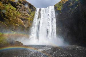 låg vinkel utsikt över vackra regnbågar och skogafoss vattenfall som faller från klippor foto