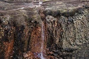 utsikt över litet vattenfall som faller över basaltstenspelare på klippan i dalen foto