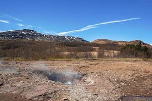 rök som avger från strokkur gejser mitt i landskapet mot blå himmel foto