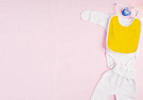 babykläder och andra saker för barn på rosa bakgrund. nyfödd baby koncept. toppvy foto