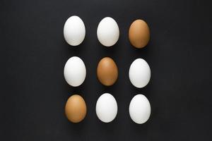 uppsättning färska kycklingägg i behållare på svart papper bakgrund. koncept för påsk med kopia utrymme. kreativ layout gjord av vita och bruna ägg. bild ovanifrån foto