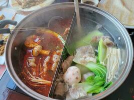 kinesisk hot pot med kryddig och vanlig buljong och kött och grönsaker foto
