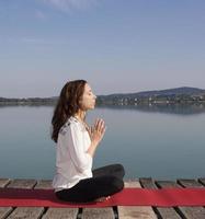 ung kaukasisk kvinna mediterar vid sjön foto