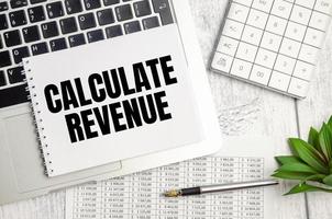 laptop diagram, penna och en vit anteckningsbok med texten beräkna intäkter foto