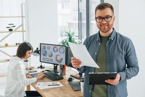 positiv man står framför kvinna som sitter vid bordet. två designers som arbetar tillsammans på kontoret foto