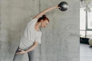 atletisk ingefärshårig ung kvinna som utför barre övning med små fitball foto