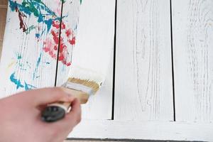 mänsklig hand som håller pensel målning vit färg på ett vitt träbord. foto