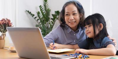 asiatisk mormor lär barnbarn att rita och göra läxor hemma. foto