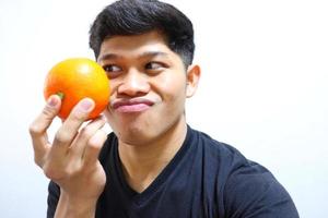 attraktiv asiatisk man äter apelsiner. isolerad på vit bakgrund foto