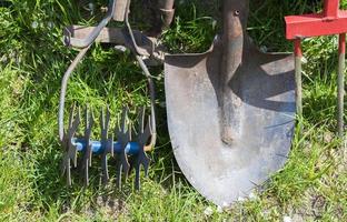 trädgårdsredskap. trädgårdsredskap på bakgrunden av en trädgård i grönt gräs. sommararbete verktyg. spade, gaffel och bakpulver staplade i trädgården utanför. begreppet trädgårdsredskap. foto