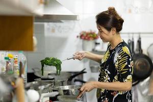 en autentisk riktig bild av asiatisk kvinna som kokar och lagar gröna grönsaker till mat i köket. foto