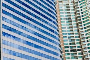 blå himmel och moln reflekteras på glaset av kontorsbyggnader i stadens centrum en ljus solig dag. foto