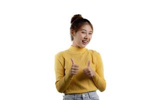 porträtt vacker asiatisk kvinna i en gul skjorta står, höjer sin hand och visar sin tumme. porträttkoncept som används för reklam och skyltar, isolerad över den tomma bakgrunden, kopieringsutrymme. foto