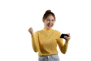 porträtt av en vacker asiatisk kvinna i en gul skjorta som spelar på en smartphone. porträttkoncept som används för reklam och skyltar, isolerad över den tomma bakgrunden, kopieringsutrymme. foto