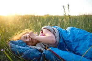 flickan är missnöjd med att klia myggbett, barnet sover i en sovsäck på gräset på en campingtur. miljövänlig friluftsliv, sommartid. sömnstörning, avstötande. foto