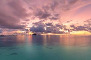 lyxiga vattenvillor resort och träbrygga. vacker himmel och moln och strand bakgrund för sommarsemester semester och resor. solnedgång landskap på maldiverna ön strand, vatten villor resort foto