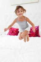 flicka hoppar på sängen bär pyjamas foto