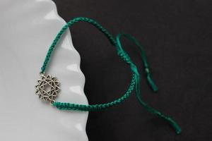 grönt flätat armband med chakra anahatha på kanten av en snövit tallrik foto