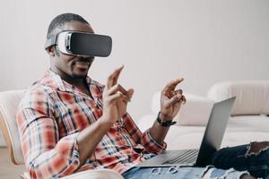 afrikansk amerikansk kille mjukvaruutvecklare i virtuell verklighetsglasögon som arbetar i cyberrymden på bärbar dator foto