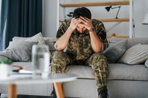 på soffan. posttraumatisk stressyndrom. soldat i uniform sitter inomhus foto