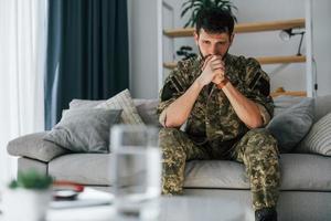 på soffan. posttraumatisk stressyndrom. soldat i uniform sitter inomhus foto