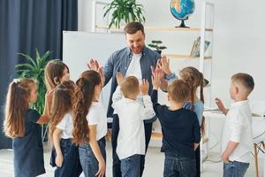 står och ger high fives. grupp barn elever i klassen i skolan med lärare foto