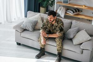 dåligt humör. posttraumatisk stressyndrom. soldat i uniform sitter inomhus foto