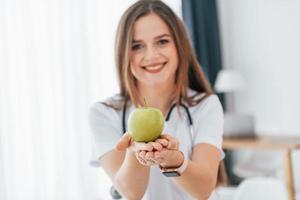 kvinna som håller ett äpple. professionell medicinsk arbetare i vit rock är på kontoret foto