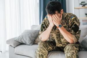 med tillbakablickar. posttraumatisk stressyndrom. soldat i uniform sitter inomhus foto