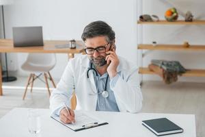 man ger information via telefon. professionell medicinsk arbetare i vit rock är på kontoret foto