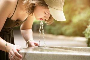 tonårsflicka dricksvatten från en utomhus vatten fontän foto