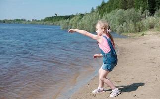 söt liten flicka kastar en sten i floden eller havet foto