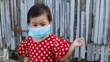 porträtt av olycklig och orolig orolig baby asiatisk flicka bär skyddande ansiktsmask stående utomhus. foto