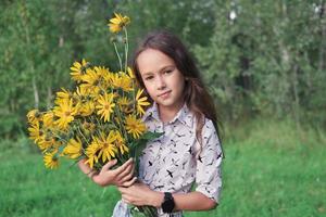 liten flicka som håller bakom en bukett topinamburblommor. foto