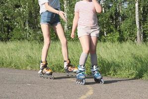 tonåringsflicka och hennes lillasyster rullskridskor i parken. delvis utsikt. sport och fritid koncept. preshcool flicka och tonåring tillbringar tid tillsammans foto