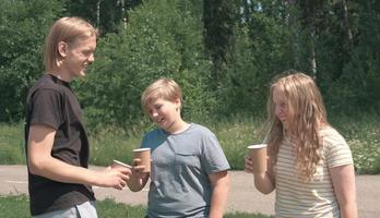 kaukasiska tonåringar har roligt dricker kaffe för att gå i en park. pratar och skrattar pojkar och flickor, en väldigt lång pojke. vänner på semester utomhus, solig sommardag. foto
