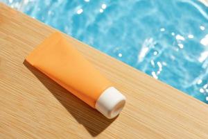 kosmetisk produkt i en orange flaska på träplanka, skönhetsspa medicinsk hudvård grädde mockup förpackning med sommarvatten pool färskt koncept. solljus i vatten foto