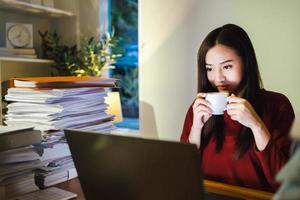 arbetsnarkoman människor koncept. asiatisk kvinna dricker kaffe under övertid på hemmakontoret foto