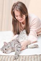 ung kvinna leker med sin tabby katt liggande på en säng. smeka husdjur försiktigt, vänskap och kärlek. foto