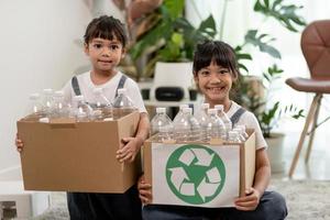 leende barn har roligt medan de segregerar plastflaskor och papper i en papperskorg foto